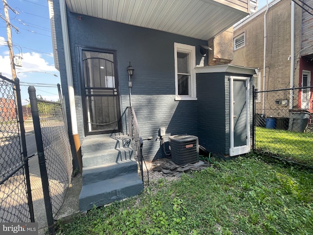 view of exterior entry featuring brick siding, fence, and central air condition unit