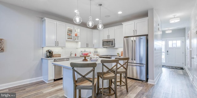 kitchen with appliances with stainless steel finishes, light hardwood / wood-style floors, white cabinetry, and decorative light fixtures