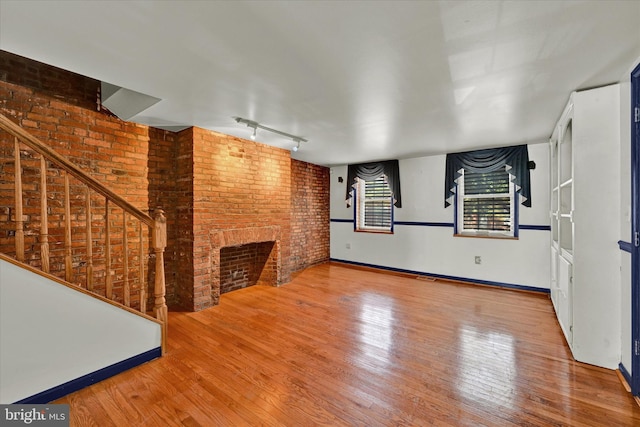 unfurnished living room with hardwood / wood-style flooring, rail lighting, a brick fireplace, and brick wall