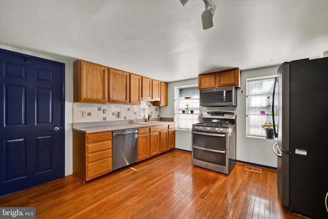 kitchen with sink, stainless steel appliances, hardwood / wood-style flooring, and backsplash