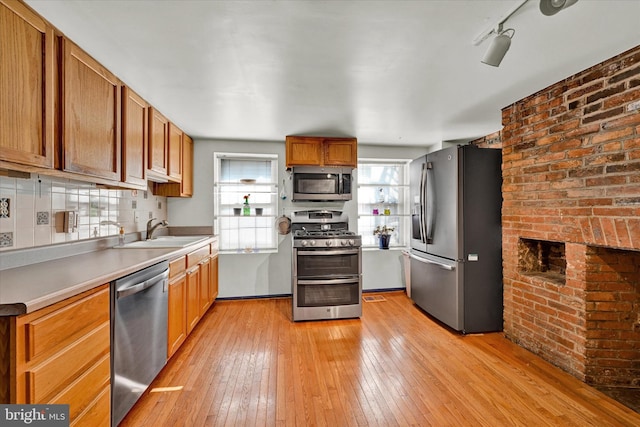 kitchen featuring backsplash, sink, appliances with stainless steel finishes, light hardwood / wood-style flooring, and brick wall