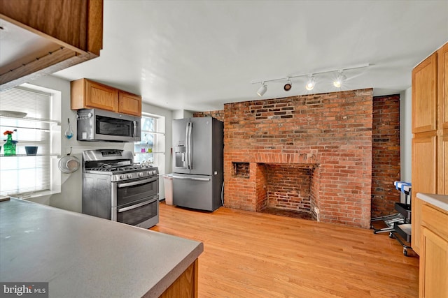 kitchen featuring appliances with stainless steel finishes, rail lighting, brick wall, light wood-type flooring, and a brick fireplace