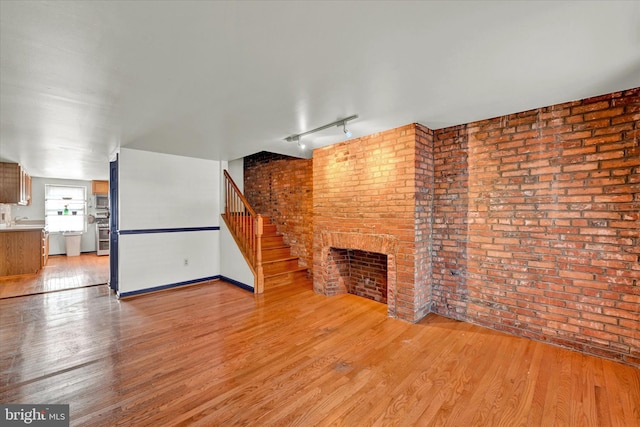 unfurnished living room featuring light hardwood / wood-style flooring, sink, brick wall, track lighting, and a brick fireplace