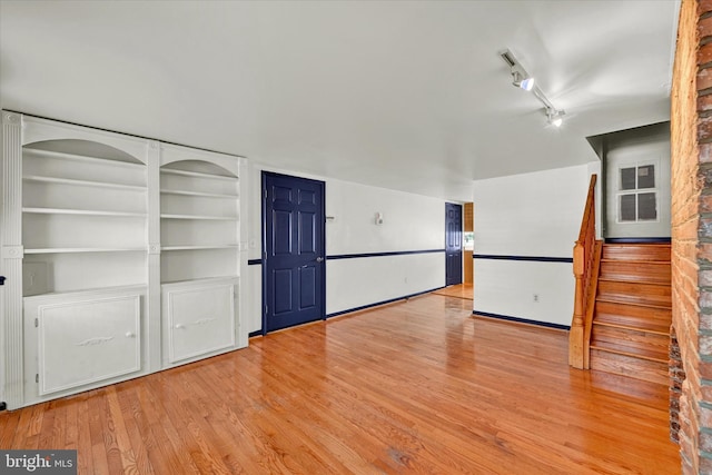 unfurnished living room with built in features, hardwood / wood-style floors, and rail lighting