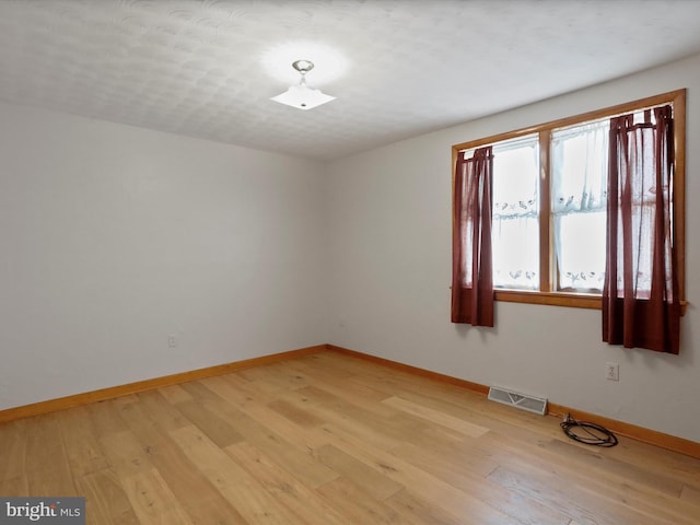 empty room with light wood-type flooring, a textured ceiling, and a healthy amount of sunlight