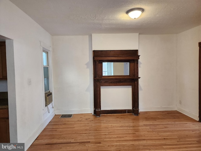 spare room with visible vents, light wood-style floors, a textured ceiling, cooling unit, and baseboards