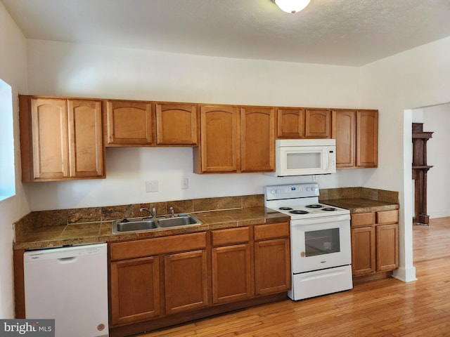 kitchen featuring white appliances, tile countertops, brown cabinets, light wood-style floors, and a sink