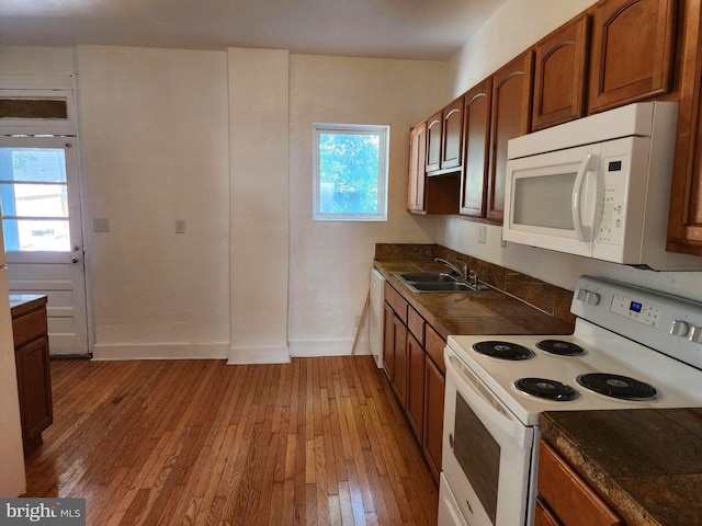 kitchen featuring white appliances, a sink, light wood-style floors, brown cabinets, and dark countertops