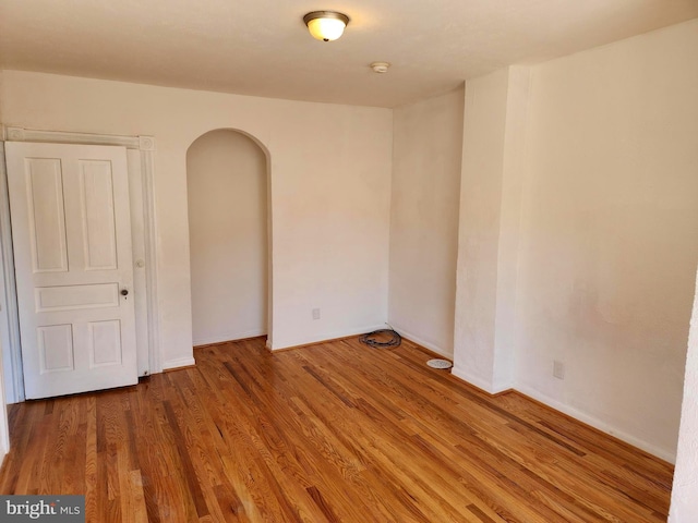 unfurnished room with arched walkways, wood finished floors, and baseboards