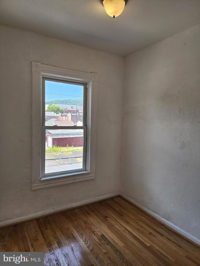 empty room featuring dark wood-style floors, a textured wall, and baseboards