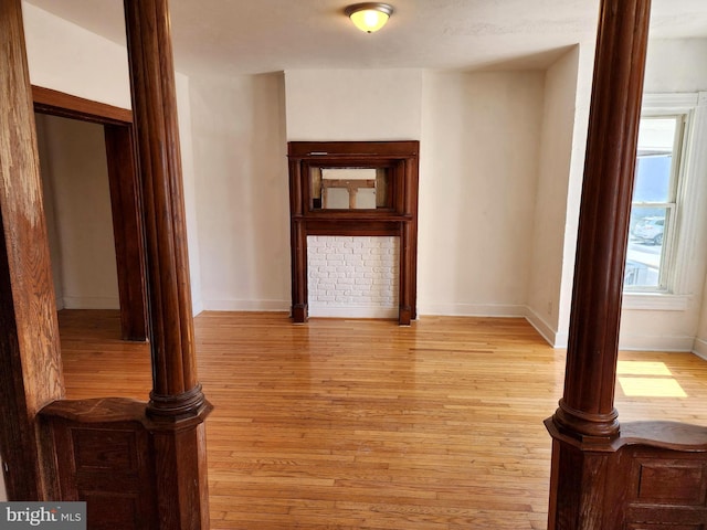 interior space featuring ornate columns, light wood-style flooring, and baseboards