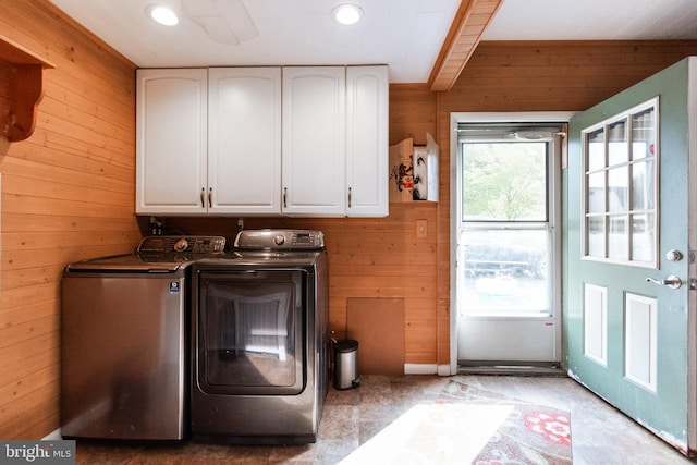 clothes washing area featuring wooden walls, washing machine and dryer, and cabinets