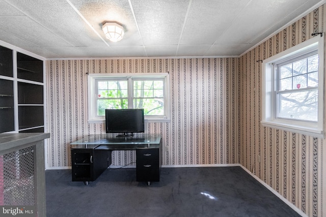 unfurnished office featuring a healthy amount of sunlight, a textured ceiling, and dark colored carpet