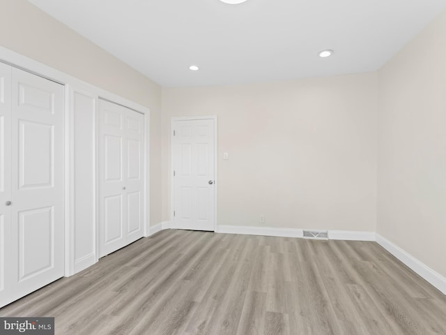 unfurnished bedroom featuring multiple closets and light wood-type flooring