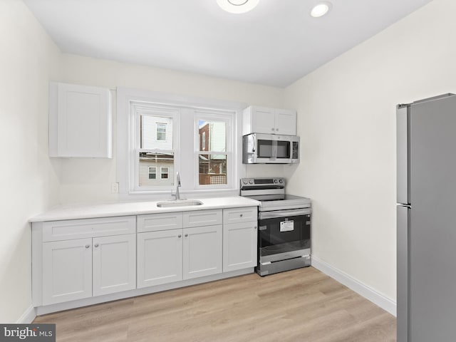 kitchen featuring stainless steel appliances, white cabinetry, sink, and light hardwood / wood-style flooring