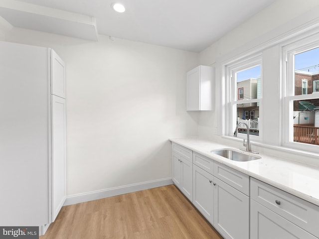 kitchen featuring white cabinetry, sink, light stone counters, and light wood-type flooring