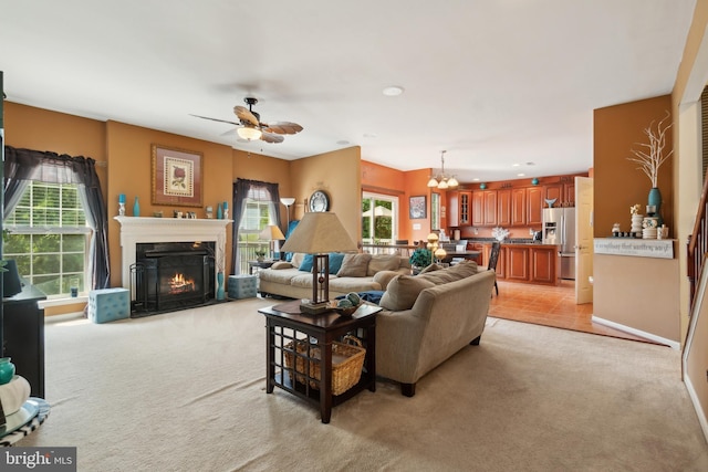 living room with light colored carpet, a wealth of natural light, and ceiling fan with notable chandelier