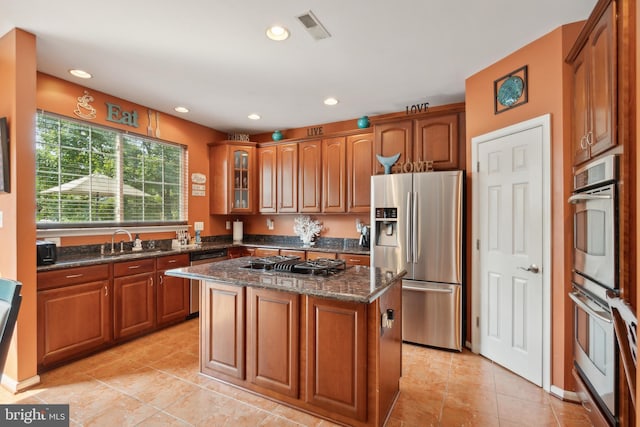 kitchen featuring stainless steel appliances, light tile patterned floors, a kitchen island, dark stone countertops, and sink