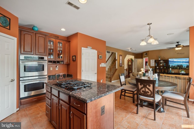 kitchen with pendant lighting, a center island, dark stone countertops, appliances with stainless steel finishes, and ceiling fan