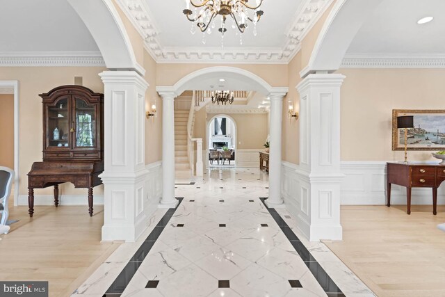 hall featuring light wood-type flooring, decorative columns, a notable chandelier, and ornamental molding