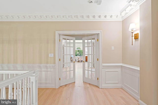 entryway featuring ornamental molding, french doors, wainscoting, and light wood finished floors