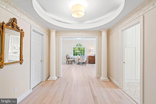 hallway featuring baseboards, a tray ceiling, light wood-type flooring, and ornate columns