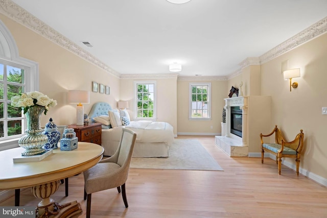 bedroom featuring baseboards, visible vents, light wood-style flooring, crown molding, and a fireplace