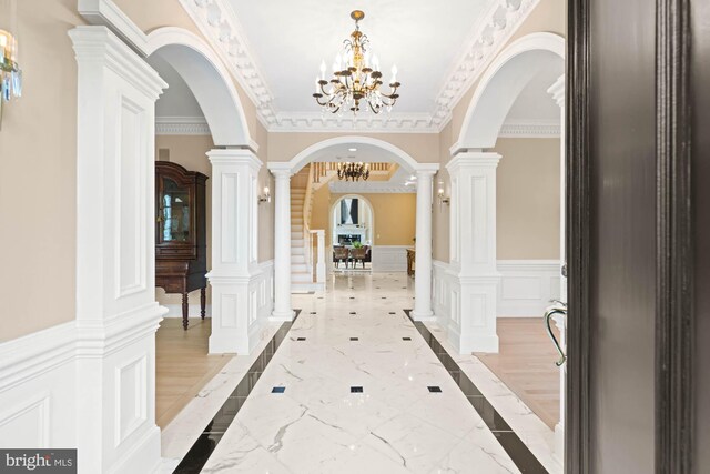 corridor featuring an inviting chandelier, crown molding, and ornate columns