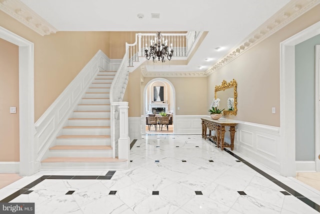 foyer entrance with marble finish floor, a decorative wall, stairway, wainscoting, and a chandelier