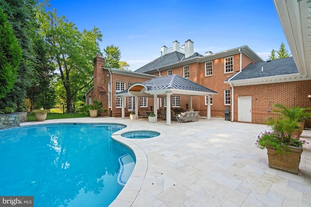 back of house with a patio area, brick siding, a pool with connected hot tub, and a chimney