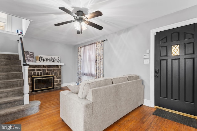 living room with ceiling fan, a stone fireplace, and hardwood / wood-style floors