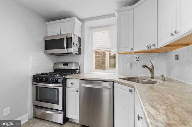 kitchen featuring tasteful backsplash, stainless steel appliances, light stone countertops, sink, and white cabinetry