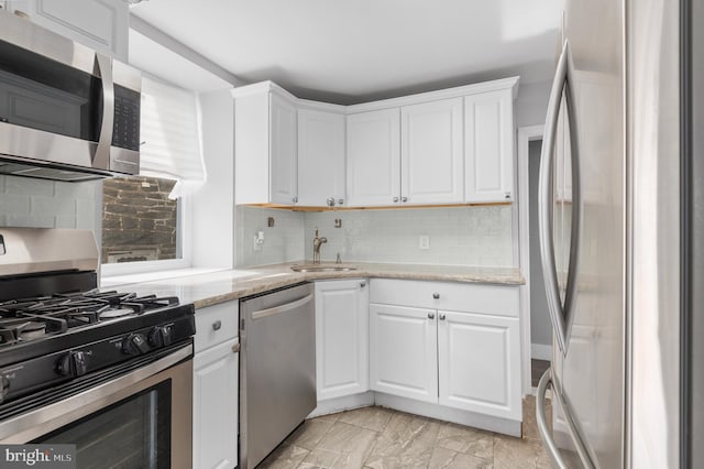 kitchen with white cabinetry, stainless steel appliances, light stone countertops, sink, and decorative backsplash