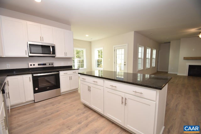 kitchen featuring a center island, appliances with stainless steel finishes, white cabinets, dark stone countertops, and light hardwood / wood-style flooring