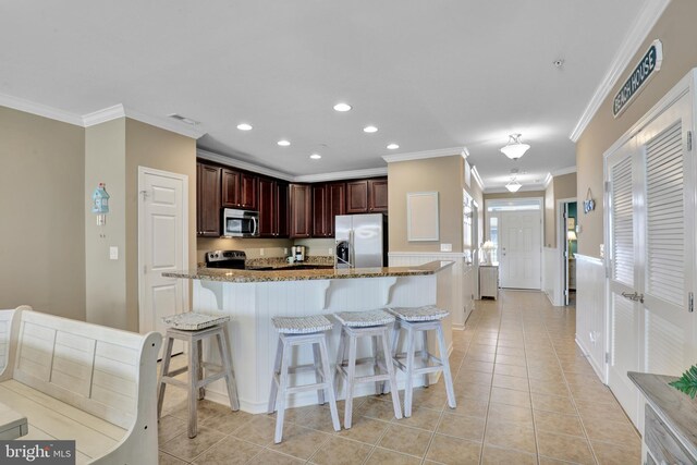 kitchen featuring appliances with stainless steel finishes, light stone counters, light tile patterned flooring, a breakfast bar area, and a center island with sink