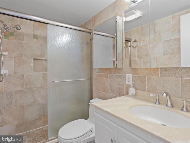 full bath featuring tiled shower, vanity, toilet, and tile walls