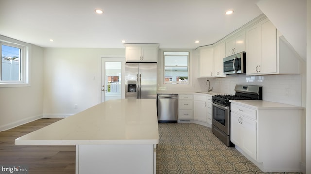 kitchen featuring a center island, stainless steel appliances, white cabinetry, wood-type flooring, and decorative backsplash