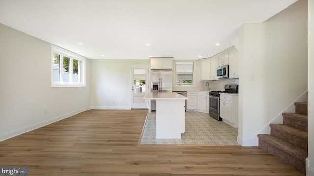 kitchen with light wood-type flooring, white cabinetry, tasteful backsplash, stainless steel appliances, and a kitchen island