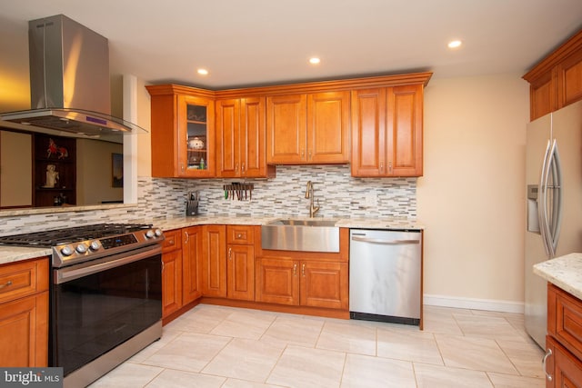 kitchen with appliances with stainless steel finishes, island range hood, tasteful backsplash, sink, and light stone countertops