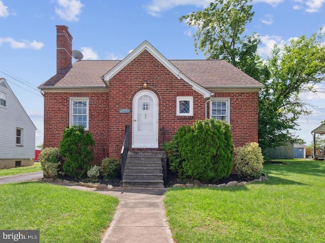 view of front of home with entry steps, brick siding, a chimney, and a front yard