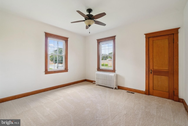 unfurnished room with radiator, ceiling fan, and light colored carpet