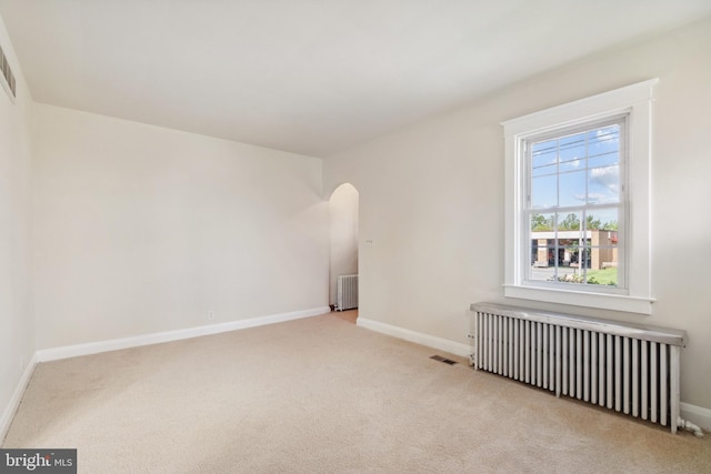 unfurnished room featuring light carpet and radiator heating unit