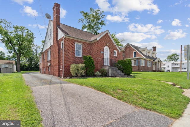 view of front of house with brick siding, a chimney, and a front lawn