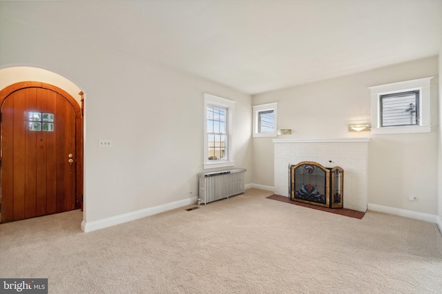 unfurnished living room with radiator heating unit, light colored carpet, and a fireplace