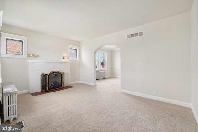 unfurnished living room featuring light carpet, a brick fireplace, and radiator heating unit