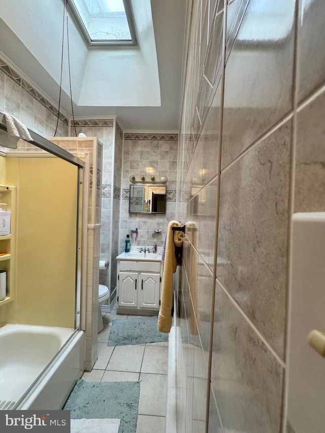 full bathroom featuring a skylight, tile walls, vanity, tile patterned flooring, and toilet