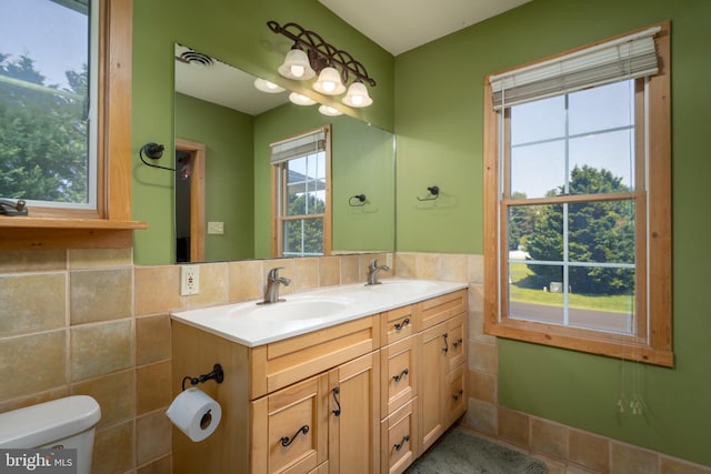 bathroom with tile walls, backsplash, dual vanity, and toilet