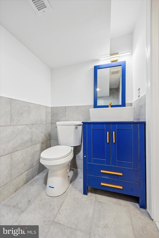 bathroom featuring visible vents, tile walls, a wainscoted wall, toilet, and vanity