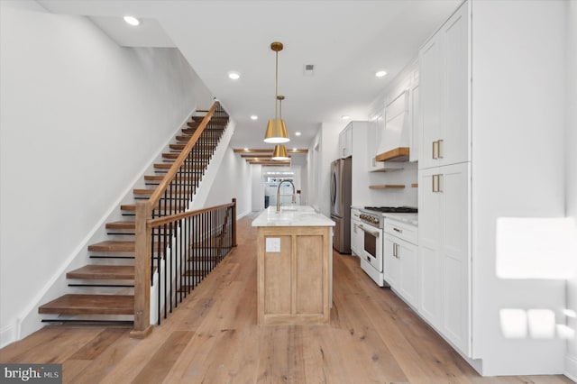 kitchen featuring white cabinetry, high end white range oven, stainless steel fridge, a center island with sink, and light wood-type flooring