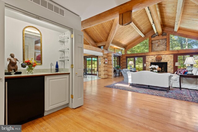 living area featuring visible vents, wooden ceiling, light wood-type flooring, wet bar, and beam ceiling